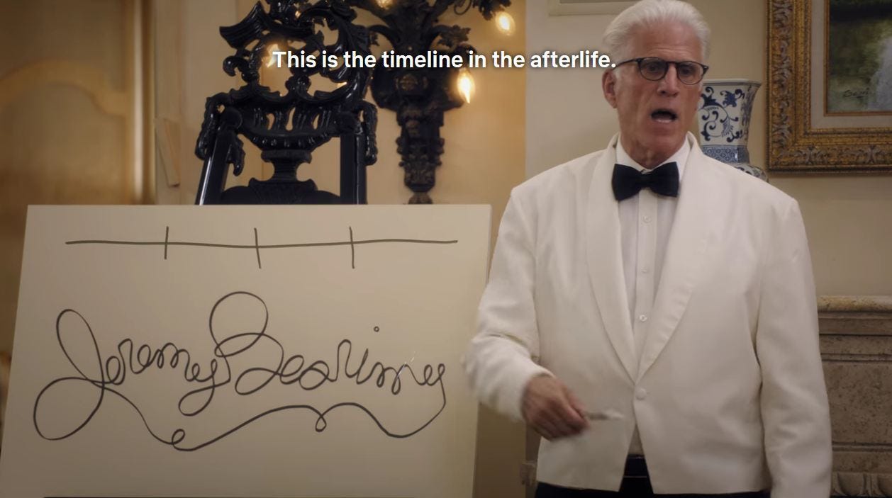 Ted Danson in a white suit stands to the right of a white paperboard sign with a resigned expression. On the sign he has drawn a straight line, and a cursive Jeremy Bearimy. The letters are all joined together with the ‘y’ of Bearimy connecting with the first ‘j’. The subtitles read: this is the timeline in the afterlife.