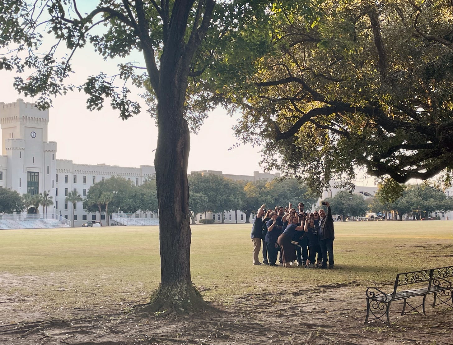 The Ogier Con Book Club poses in front of White Tower as Michael Livingston snaps a candid from his car. Trees and bench in foreground.