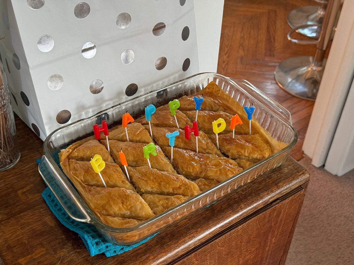 A glass pan of baklava with multicolored letter candles spelling happy birthday.