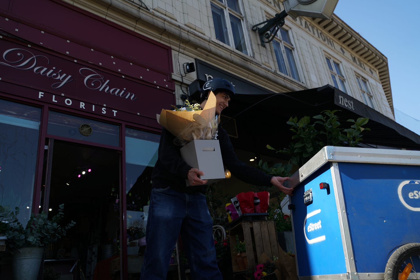 A cyclist courier picks up flowers from a local Daisy Chain florist in Willesden Green, capturing hyperlocal delivery, independent retail, and zero emission logistics in action.