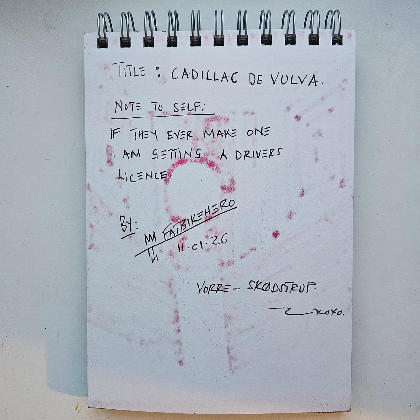 Alt Text: The back of a sketchbook page with handwritten text in black ink, showing red marker bleed-through from the front. The text reads "TITLE: CADILLAC DE VULVA" and "NOTE TO SELF: IF THEY EVER MAKE ONE I AM GETTING A DRIVERS LICENCE." Signed "BY: FATBIKEHERO," dated "11.01.26," and located "VORRE - SKØDSTRUP."