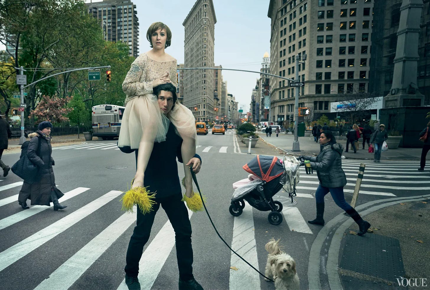 A young Lena Dunham sits atop a young Adam Driver's shoulders as he walks a Pomeranian across a busy Manhattan steet