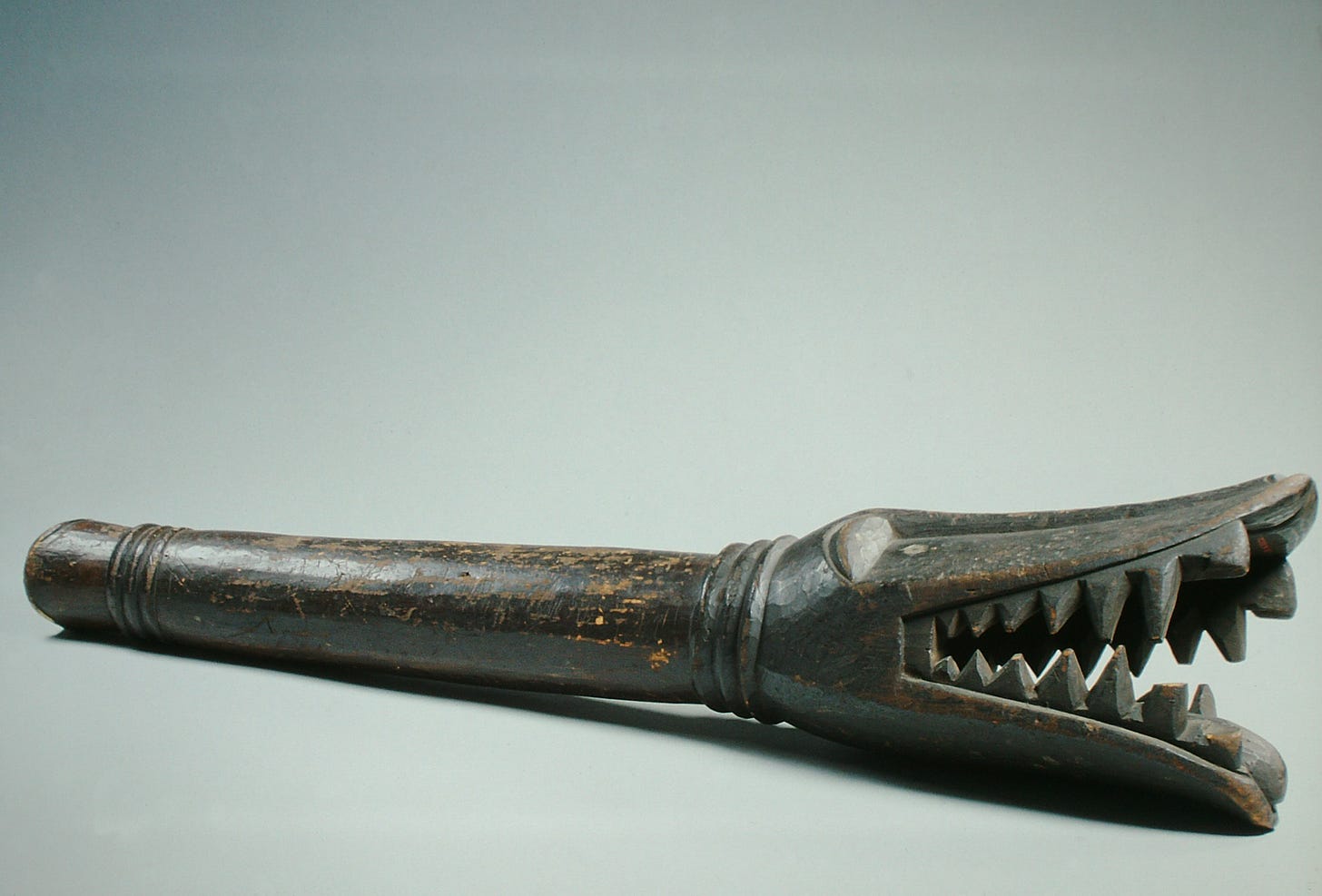 18th century Congolese wood megaphone with transforming mask motif. In profile, the voice disguiser is a ferocious crocodile but from the front it is an ancestor spirit.