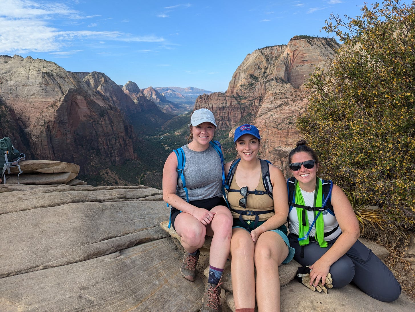 Three women smiling at the summit of Angel's Landing with a view of Zion Canyon behind them