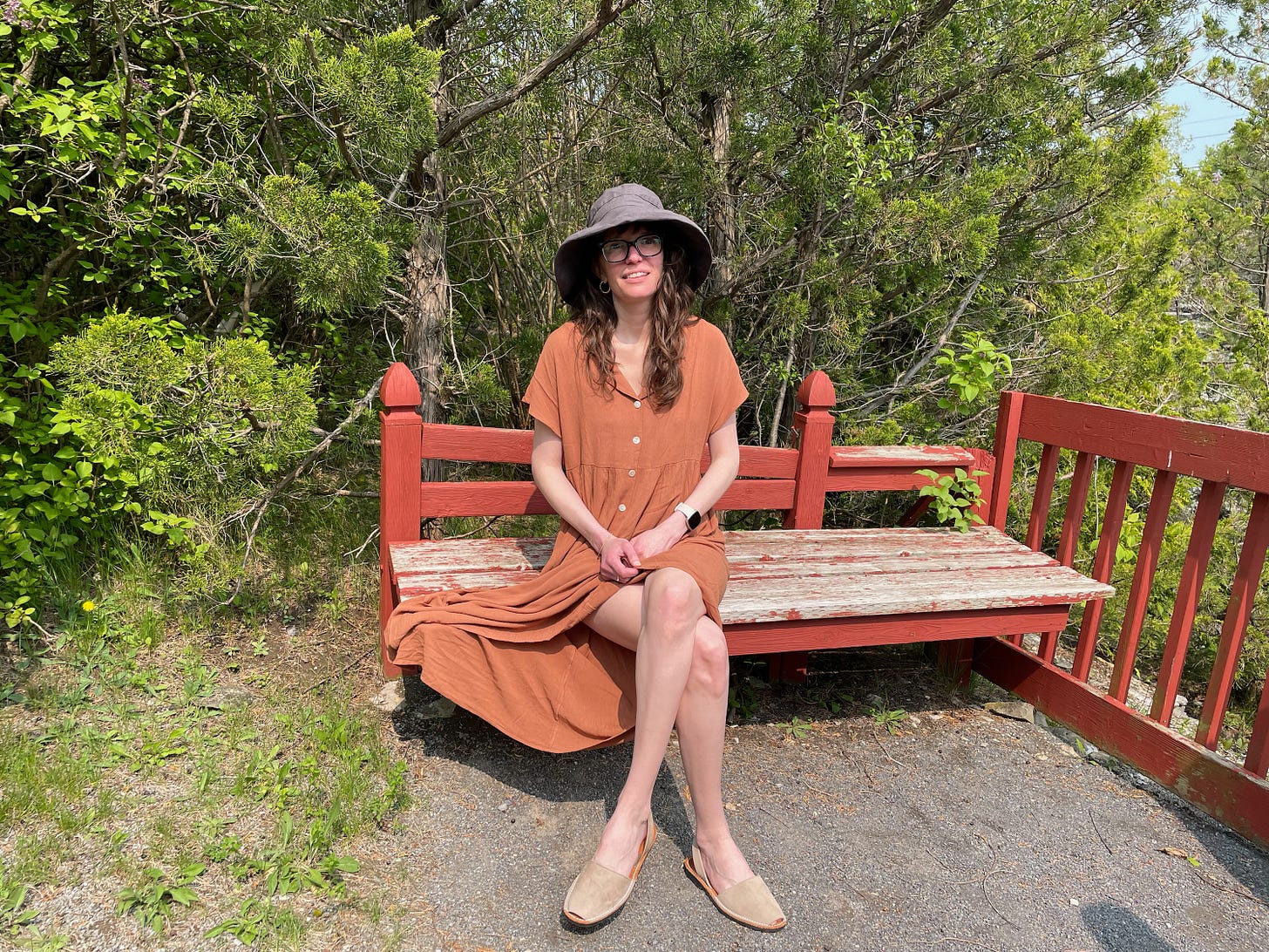 a woman with long brown hair in a blue hat and orange dress sits on a bench