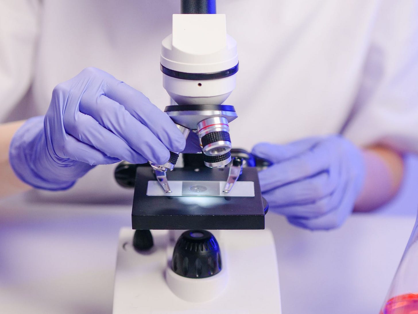 Photo by Kindel Media on Pexels Scientist wearing gloves using a microscope in a laboratory setting. (stock photo)