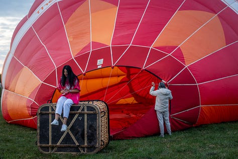 Înainte ca baloanele să urce, totul începe jos, pe iarbă, în frigul subțire al dimineții sau în lumina care abia se stinge peste câmp. Oamenii își ocupă locurile, verifică arzătoarele, întind pânza, ridică nacela, privesc cerul și, mai ales, ascultă vântul. În jur, mașinile stau cu farurile aprinse.