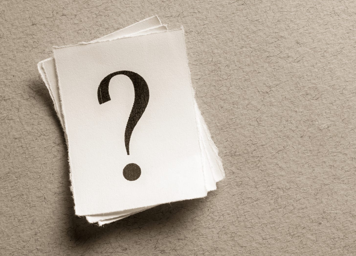 Stack of textured paper cards with a large black question mark on top, set against a neutral background with ample empty space. Stack of textured paper cards with a large black question mark on top, set against a neutral background with ample empty space.