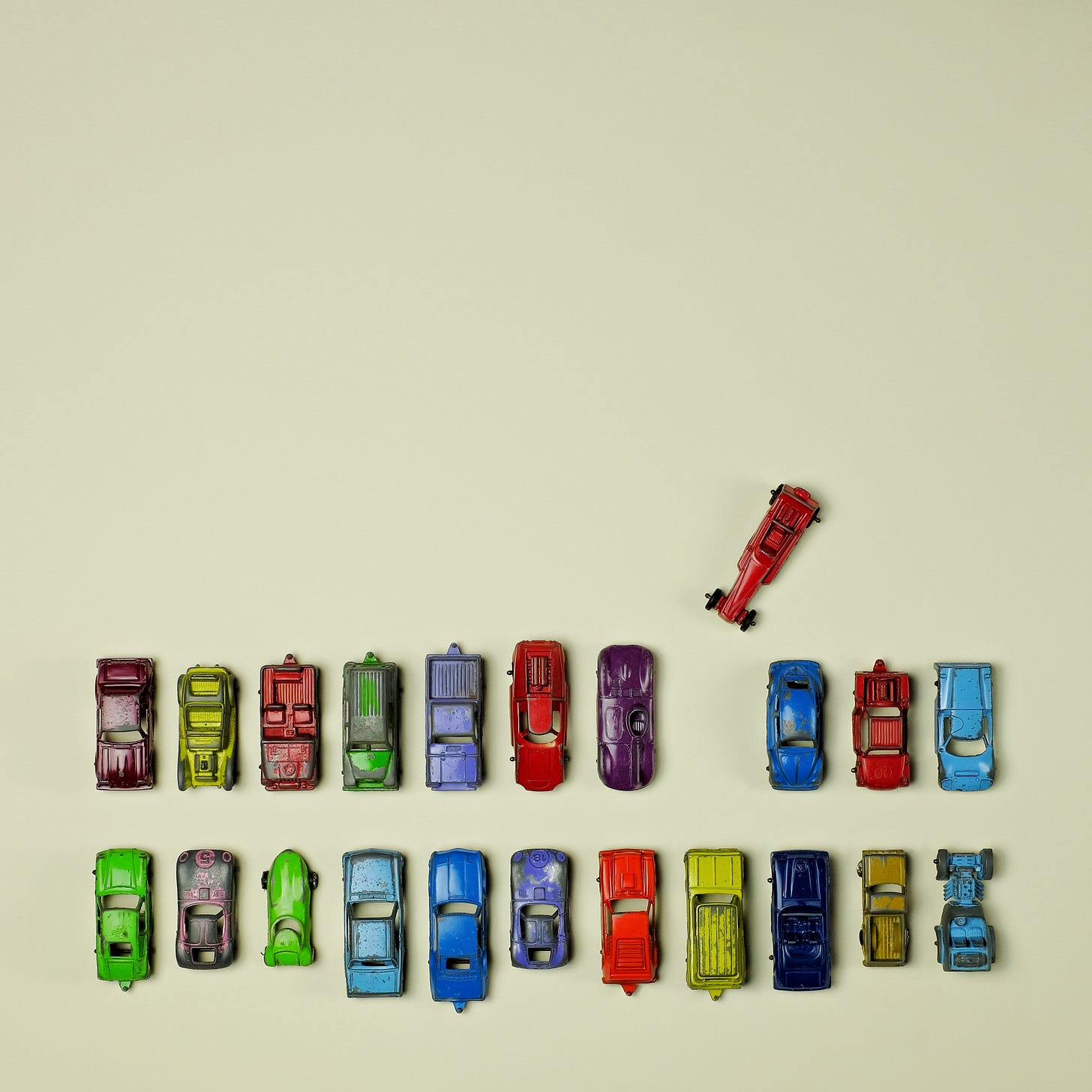 Two lines of toy metal cars with one red dragster out of its spot in line at an angle