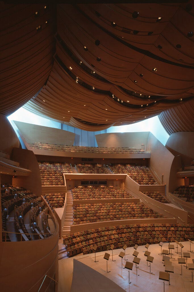 A wide interior view of a concert hall with warm colors and wood in swooping shapes.