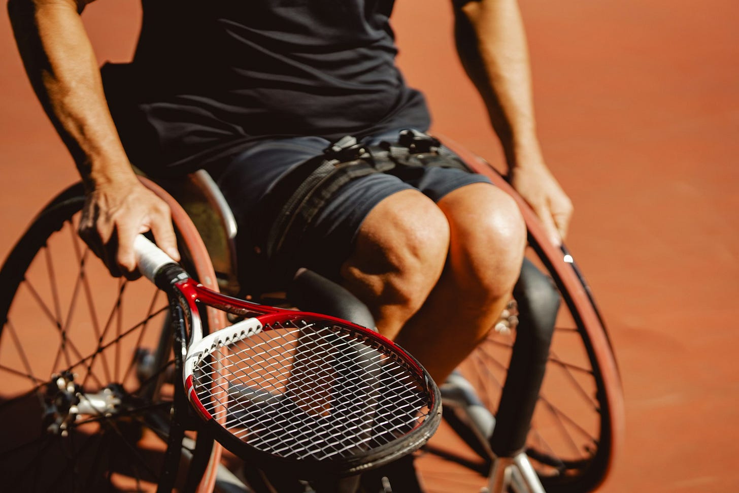 A close-up of a wheelchair tennis player gripping a racquet on a sunlit court, symbolising strength, resilience, and movement despite physical limitations.
