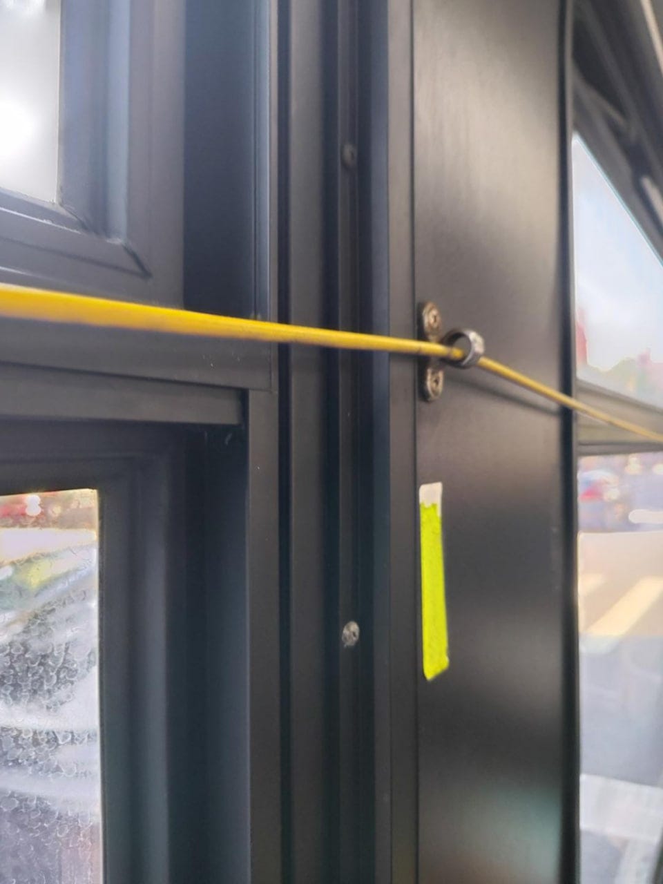 Cordón amarillo que atraviesa una guía metálica junto a la ventanilla de un autobús