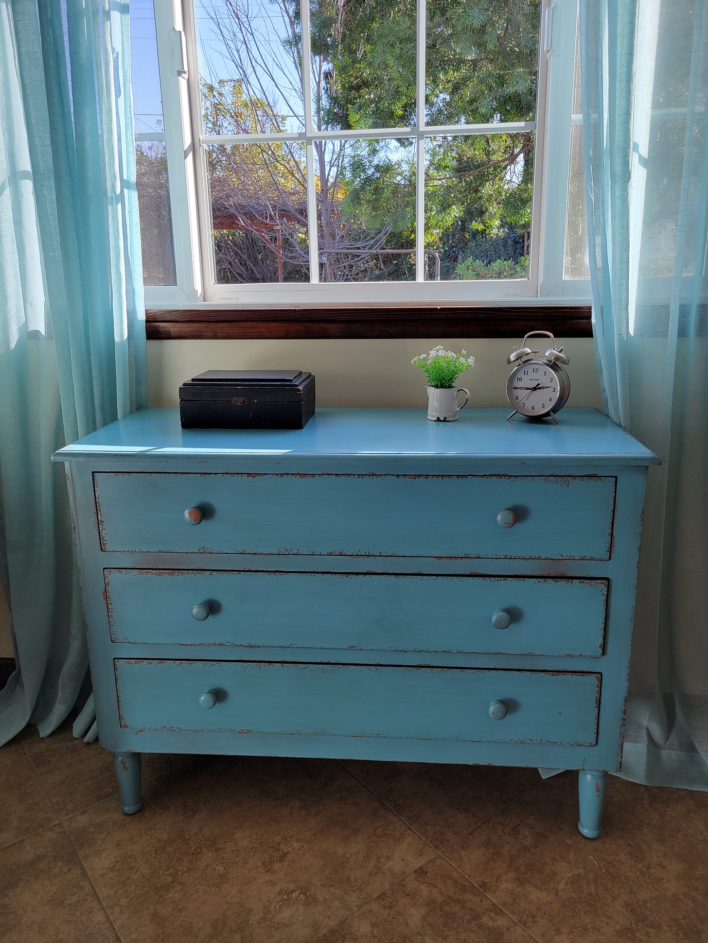 Bureau drawers chipped paint under window blue gauze drapes