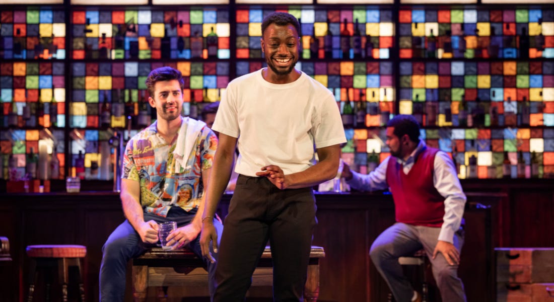 Three men on stage with one in the middle smiling, with colourful glass behind them Three men on stage with one in the middle smiling, with colourful glass behind them