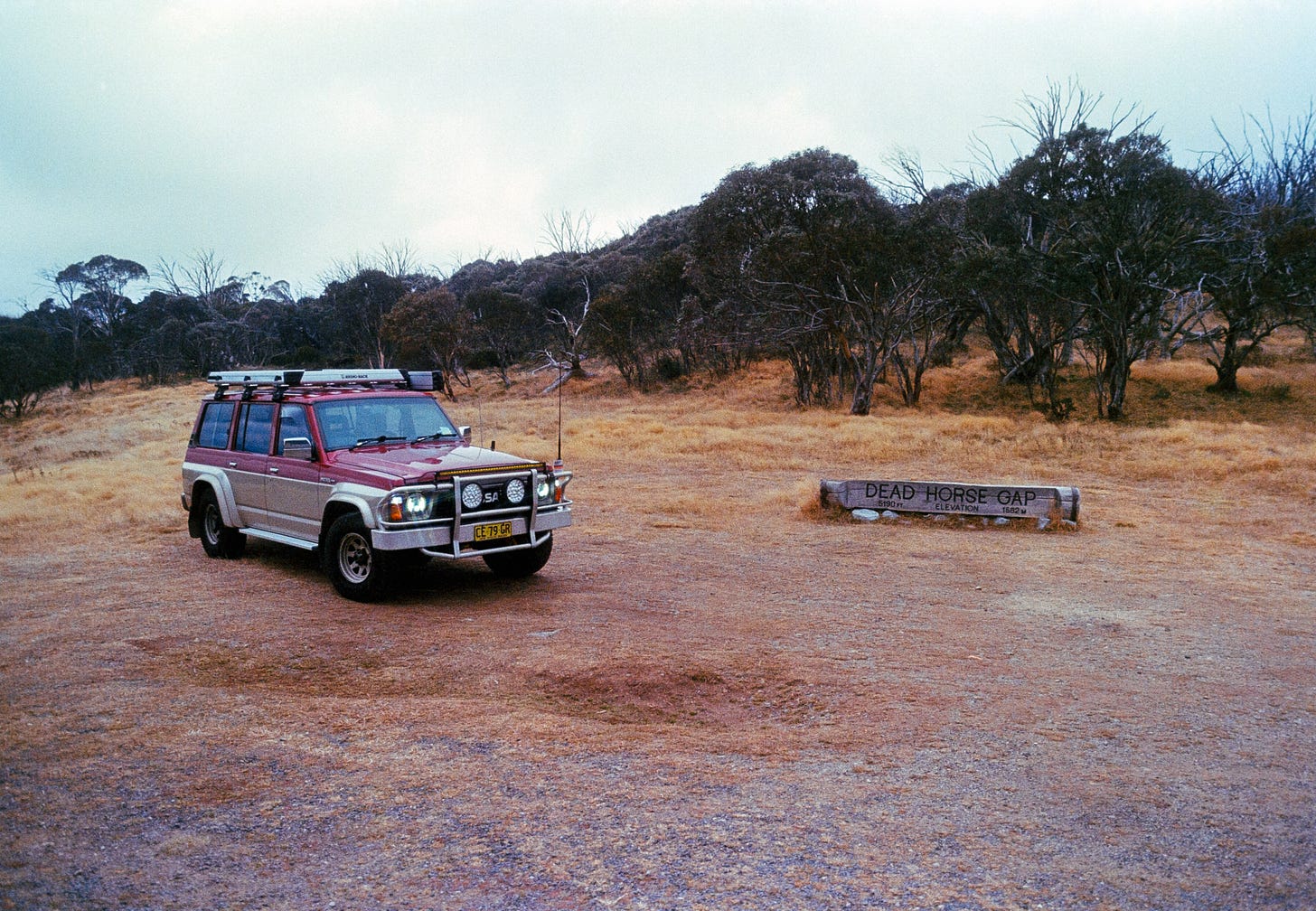 An image of Scorpion, Josie’s 4WD out in a field past Jindabyne during a storm. Scorpion is on the left with her headlights on sparkling, there’s a sign to the right of her, surrounded by trees, that says ‘Dead Horse Gap’