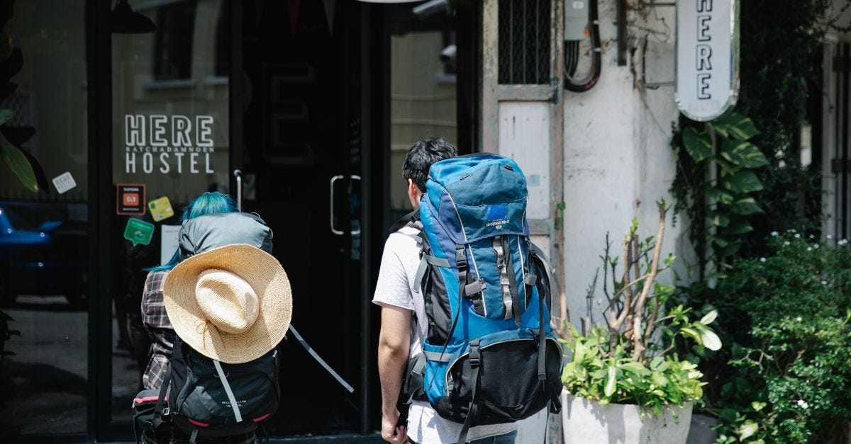 Photo: George Pak / Pexels Two backpackers stand at the entrance of a modern hostel, ready for adventure.