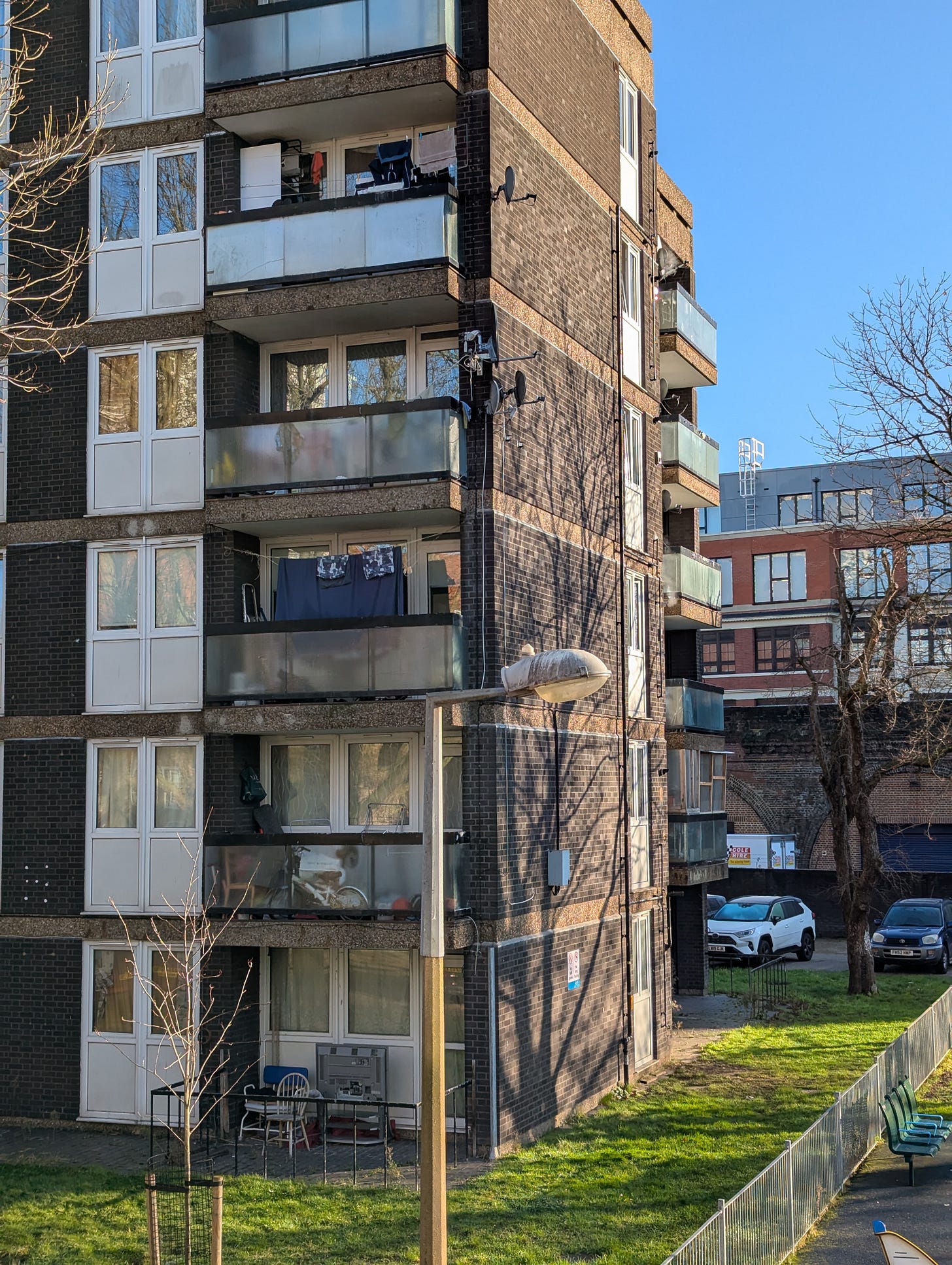 A tower block in South London, with clothes hanging to dry on balconies, and the shadow of a bare tree against one of its sides.
