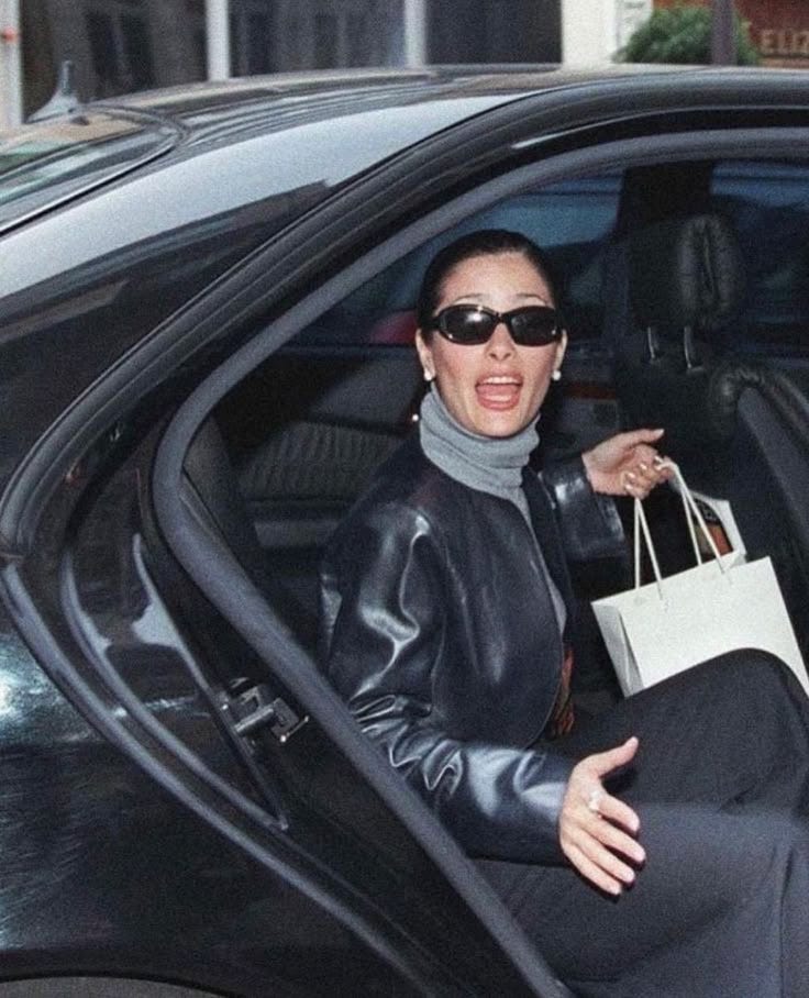 This may contain: a woman sitting in the driver's seat of a car holding onto a shopping bag