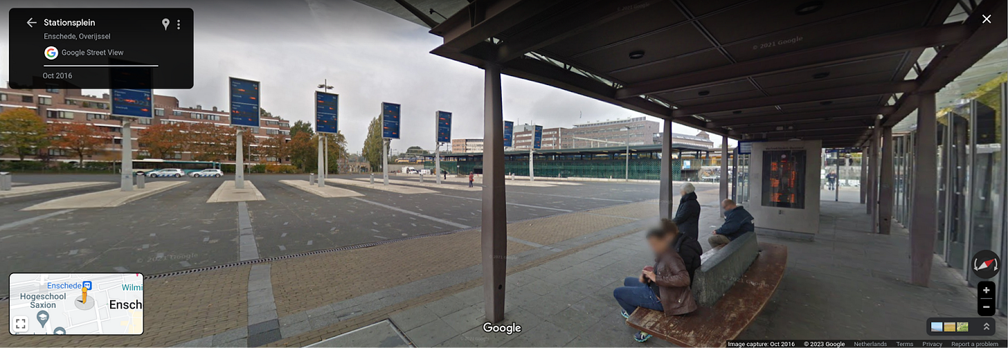 The bus station in Enchede, a line of bus platforms is visible, each one only has a large vertical sign with route and ETA information, seating is provided in a large plaza perpendicular to all the platforms.
