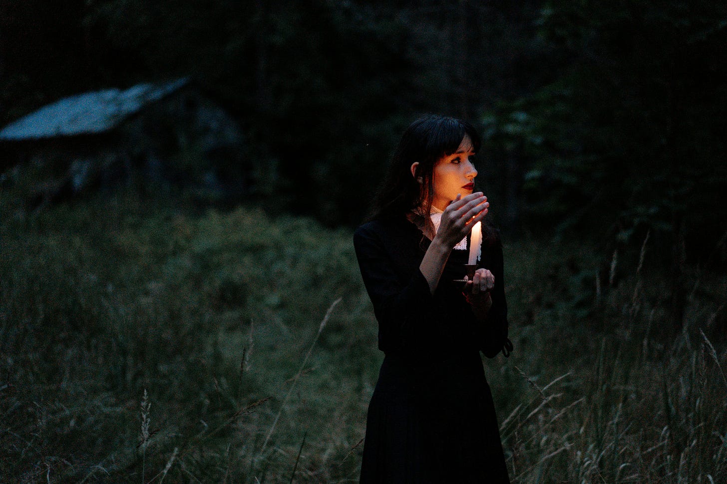 A woman walking in a dark landscape at night holding a candle