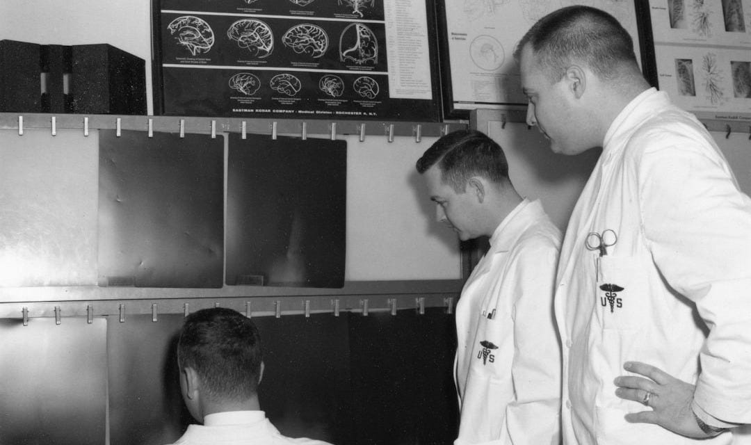 Three men in lab coats examine medical scans Three men in lab coats examine medical scans