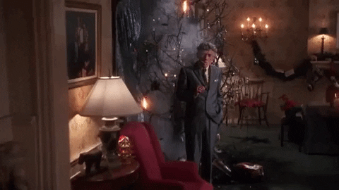 Scene from Christmas Vaction. The Christmas tree smoulders after a fire, an elderly man stands in front, also smouldering smoking a cigar