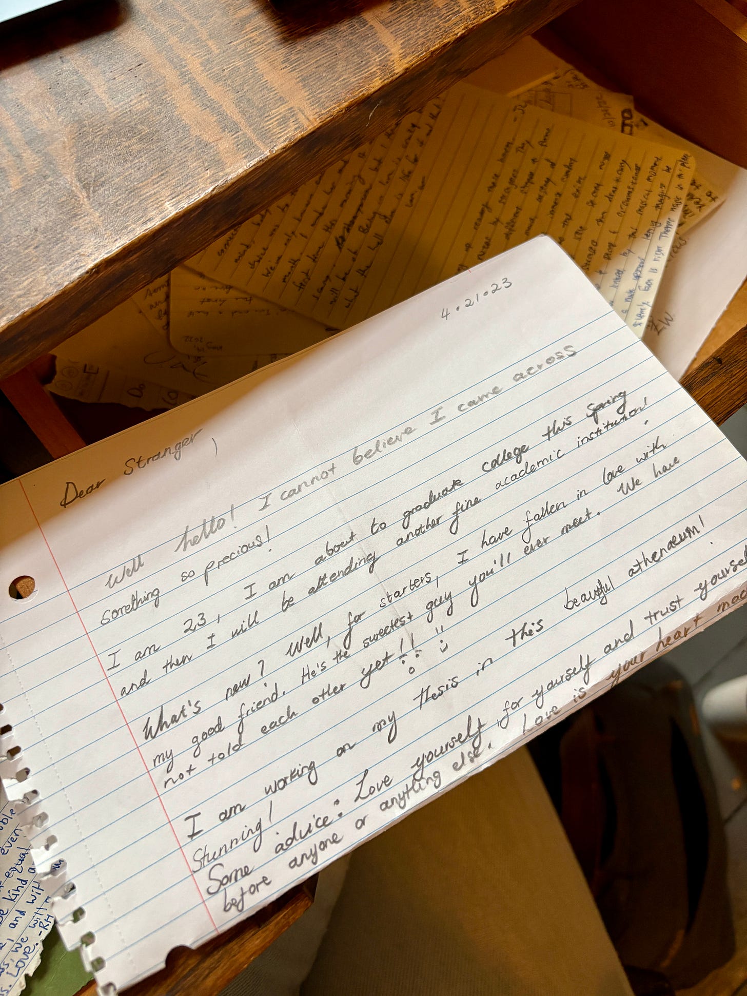 A letter on folded looseleaf paper, written in pencil, rests on an open desk drawer. It reads: 4/21/23 Dear Stranger, Well hello! I cannot believe I came across something so precious! I am 23, I am about to graduate college this spring, and then I will be attending another fine academic institution! What’s new? Well, for starters, I have fallen in love with my good friend. He’s the sweetest guy you’ll ever meet. We have not told each other yet!! :-) I am working on my thesis in this beautiful athenaeum! Stunning! Some advice: Love yourself for yourself and trust yourself before anyone or anything else. Love is in your heart A letter on folded looseleaf paper, written in pencil, rests on an open desk drawer. It reads: 4/21/23 Dear Stranger, Well hello! I cannot believe I came across something so precious! I am 23, I am about to graduate college this spring, and then I will be attending another fine academic institution! What’s new? Well, for starters, I have fallen in love with my good friend. He’s the sweetest guy you’ll ever meet. We have not told each other yet!! :-) I am working on my thesis in this beautiful athenaeum! Stunning! Some advice: Love yourself for yourself and trust yourself before anyone or anything else. Love is in your heart