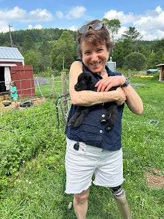 Me, holding a small black baby goat, whose legs are dangling below my forearm. Me, holding a small black baby goat, whose legs are dangling below my forearm.