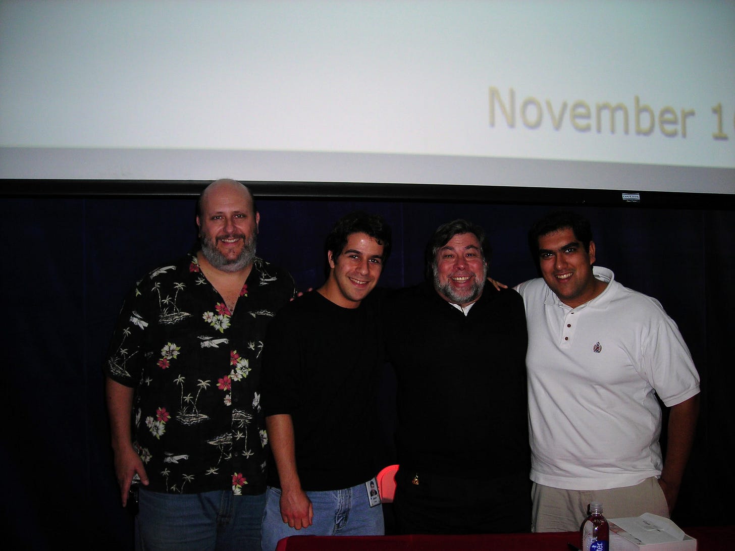 A photo taken after Woz's talk at Google in 2006. Scott Knaster, Jason Costa, Steve Wozniak, and Annand Sharma, standing onstage below a large projection screen that reads "November 1" (the rest of the date is out of frame). I'm wearing a crazy shirt and I don't know what has become of it. A photo taken after Woz's talk at Google in 2006. Scott Knaster, Jason Costa, Steve Wozniak, and Annand Sharma, standing onstage below a large projection screen that reads "November 1" (the rest of the date is out of frame). I'm wearing a crazy shirt and I don't know what has become of it.