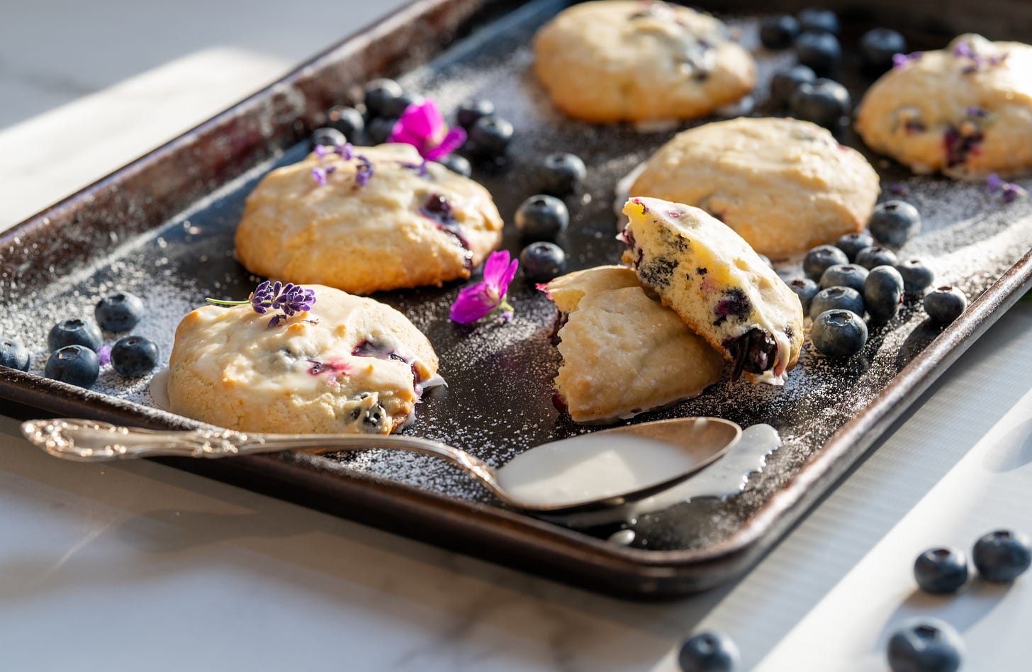 Blueberry lemon Cake Cookies on a baking pan with a spoon of lemon powdered sugar glaze