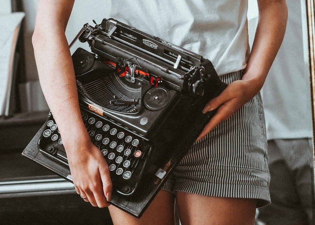 man in white crew neck t-shirt holding black typewriter