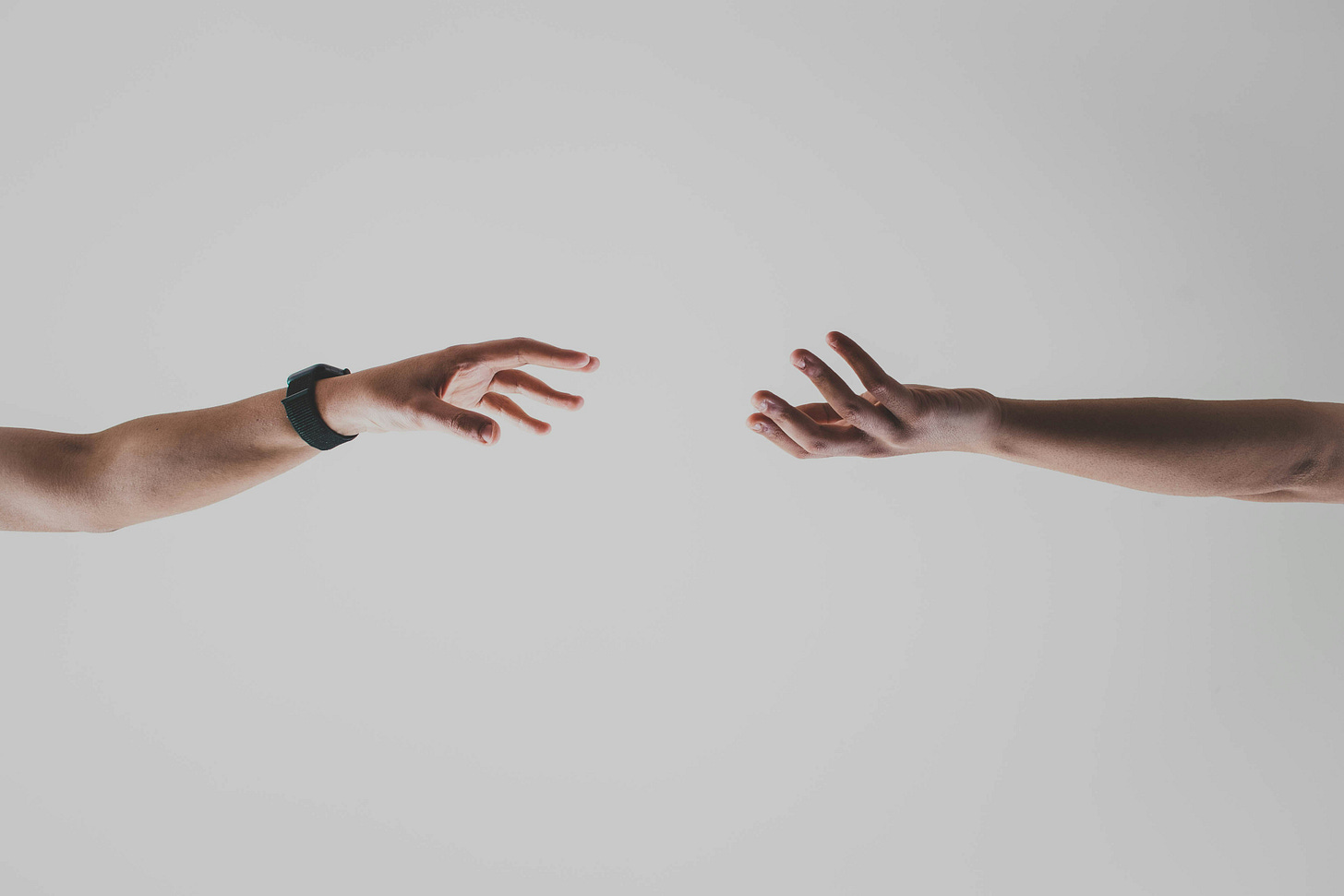 Two hands reaching across a blank space towards one another.