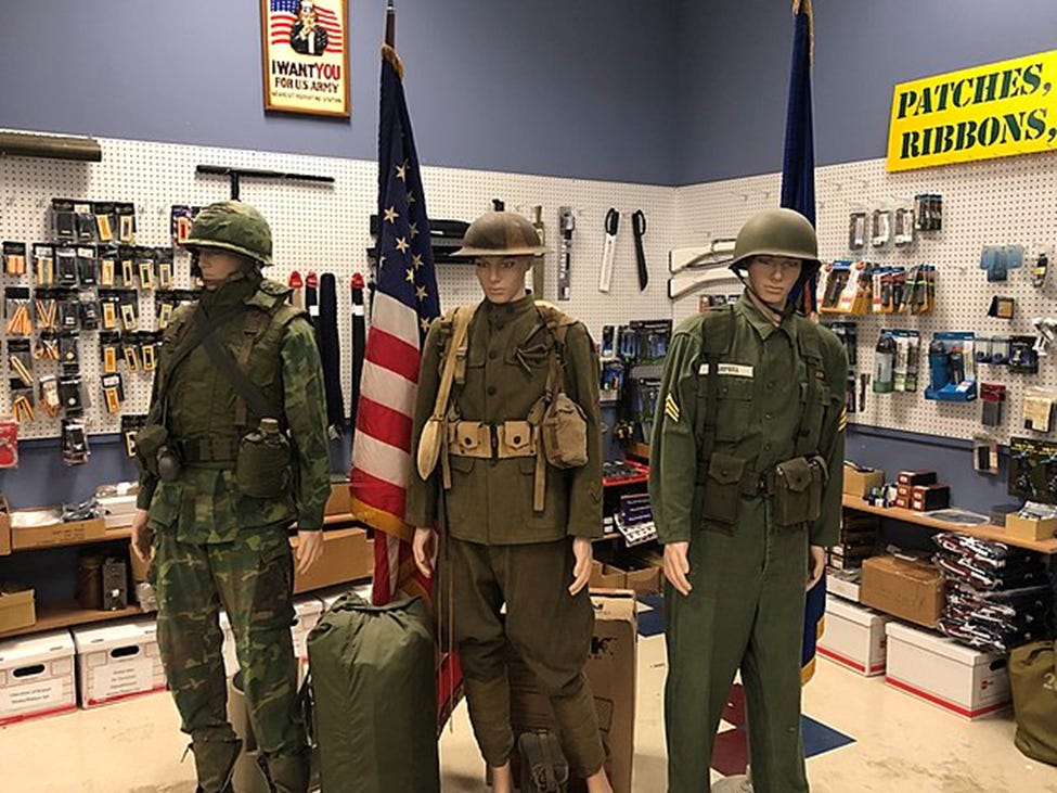 Three store mannequins dressed in military surplus uniforms standing near an American flag.