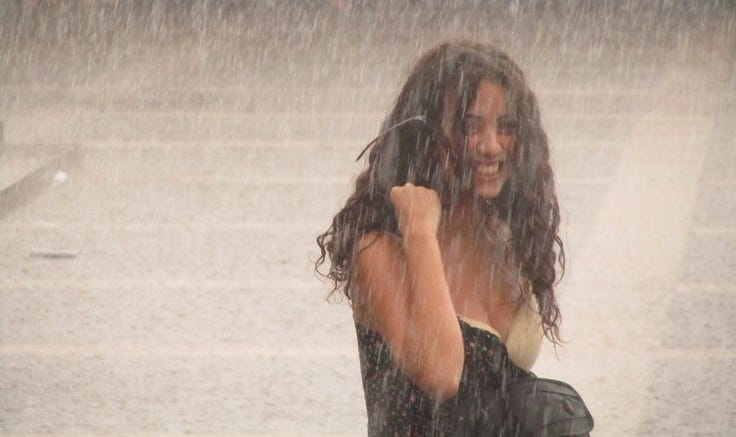 This may contain: a woman standing in the rain talking on her cell phone This may contain: a woman standing in the rain talking on her cell phone