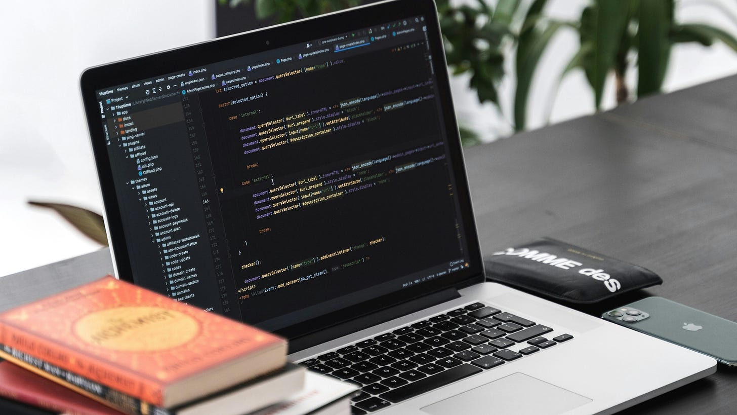 Open laptop displaying code on a dark-themed IDE, surrounded by a programming book, iPhone, and modern workspace decor, symbolizing a productive coding environment.