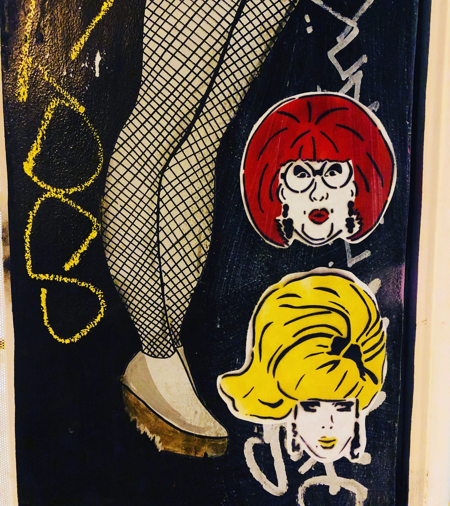 Street art features fishnet-clad legs with graffiti and two illustrated faces beside it: one with red hair, other with blonde hair. Urban vibe. The two faces are Jeremy's work of 2 drag queens, one of them being Lady Bunny. The drag queen on top has a red bob and dangly earrings with red lipstick and circular glasses. The drag queen on the bottom has big yellow hair, with a black bow in it, and pink lips, with dangly earrings. Street art features fishnet-clad legs with graffiti and two illustrated faces beside it: one with red hair, other with blonde hair. Urban vibe. The two faces are Jeremy's work of 2 drag queens, one of them being Lady Bunny. The drag queen on top has a red bob and dangly earrings with red lipstick and circular glasses. The drag queen on the bottom has big yellow hair, with a black bow in it, and pink lips, with dangly earrings.