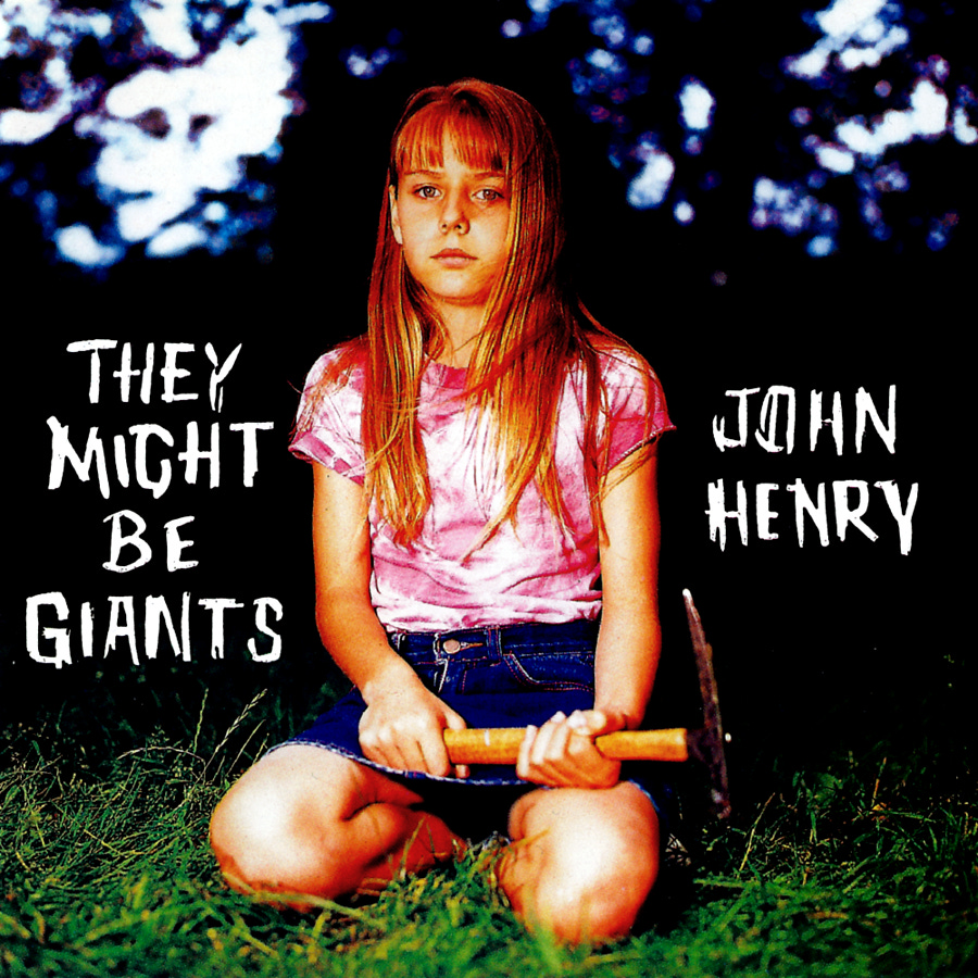 Album cover of They Might Be Giants’ 1994 record John Henry, showing a young girl with long hair and bangs, sitting in the grass with a hammer in her hands. She wears a pink tie-dye shirt and denim shorts, staring blankly at the camera against a dark background with blurred tree shapes.