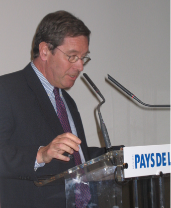 A person in a suit speaking at a podium

Description automatically generated