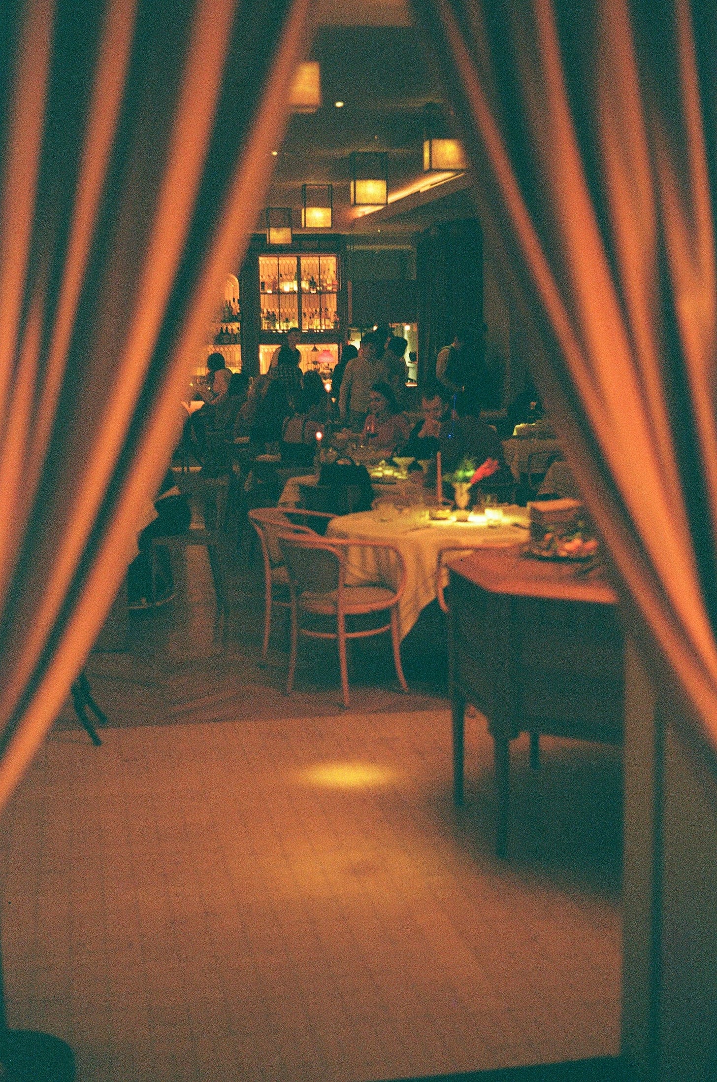 Two red curtains open into a busy dark dining room with many tables occupied by people. An amber bar can be seen at the furthest wall.