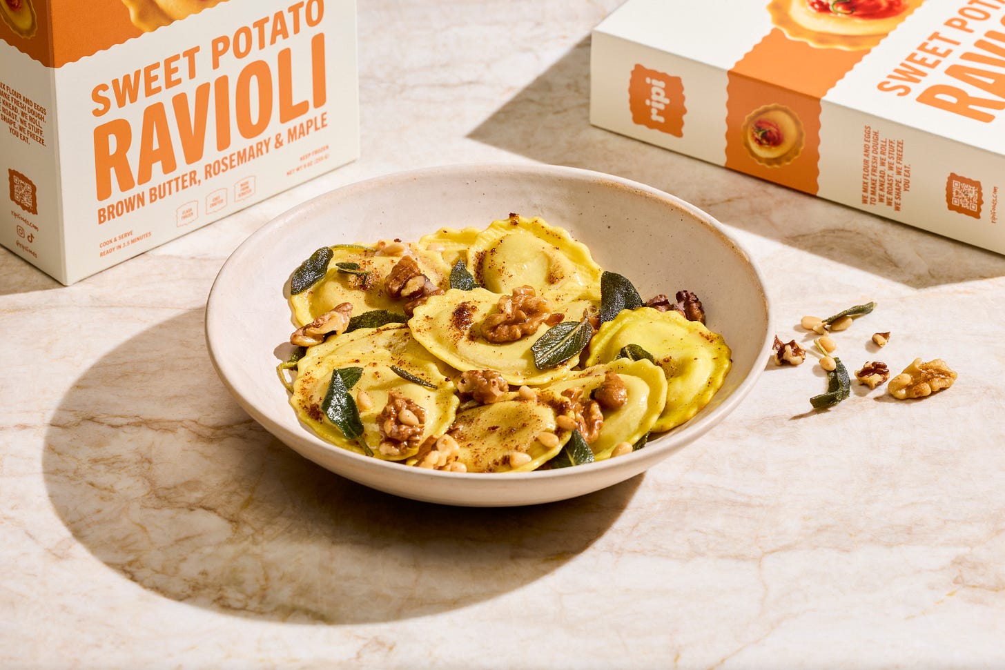 Ripi sweet potato ravioli boxes and ravioli in a white bowl with walnuts