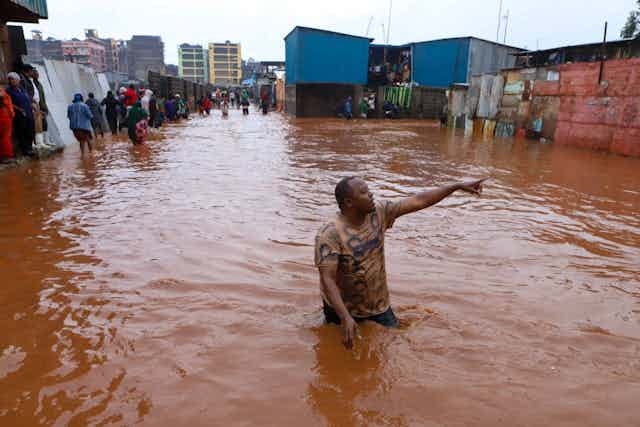A man wading in the middle of a pool of muddy water and pointing at something, while several other people are seen standing off to the side. A man wading in the middle of a pool of muddy water and pointing at something, while several other people are seen standing off to the side.