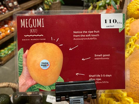 Signs and displays of unusual mango varieties at a grocery store in northern Thailand, including Megumi and Tsuya mangos.