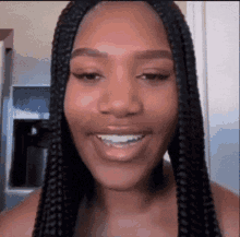 a woman with braids is smiling for the camera in a kitchen . a woman with braids is smiling for the camera in a kitchen .