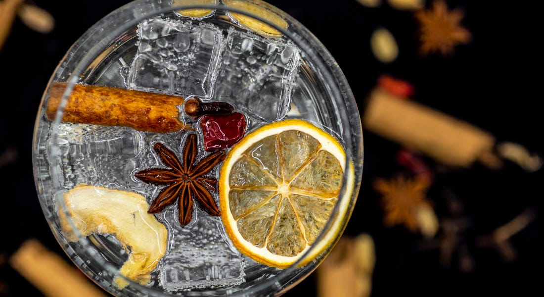 A birds eye shot of a glass of gin with lemon and spices in it, with decorations in the background