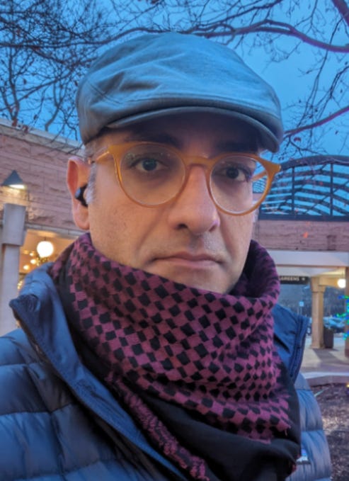 First image: A man with short dark hair and beard wearing orange-tinted round glasses, a gray flat cap, a multicolored checkered scarf, and a dark blue puffer jacket stands outdoors at dusk near brick buildings with arched structures and lit lamps, bare trees in background. Second image: A poster featuring the Palestinian flag at top, title Liberatory Violence in large red letters, a young muscular shirtless man raising his arm dynamically, smaller text discussing oppressed peoples struggles for liberation incorporating violent tactics from 18th century slave rebellions to anticolonial revolutions, course examination by Professor Alireza Doostdar including Nat Turner, French Revolution, and Palestinian revolution against Zionist settler colonialism, apartheid, and genocide.