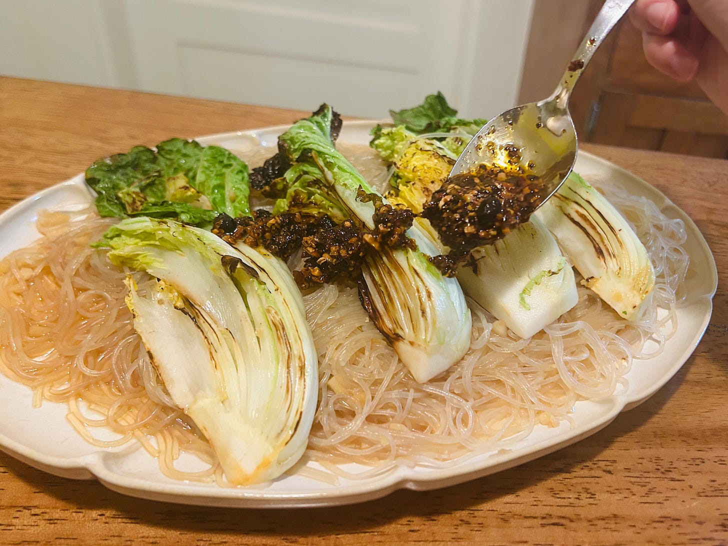 Someone uses a spoon to drizzle chili crisp onto the cabbage and noodle dish.