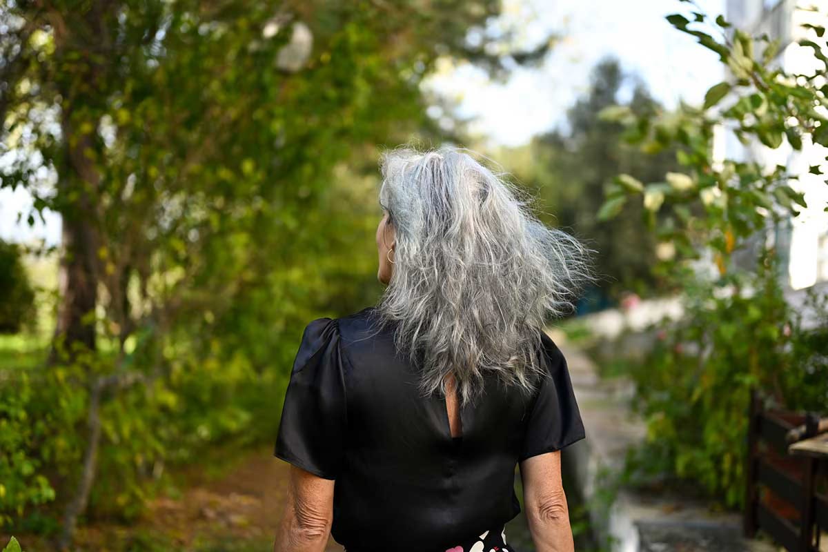 Middle-aged woman with gray hair walking outdoors on a leafy path, photographed from behind Middle-aged woman with gray hair walking outdoors on a leafy path, photographed from behind