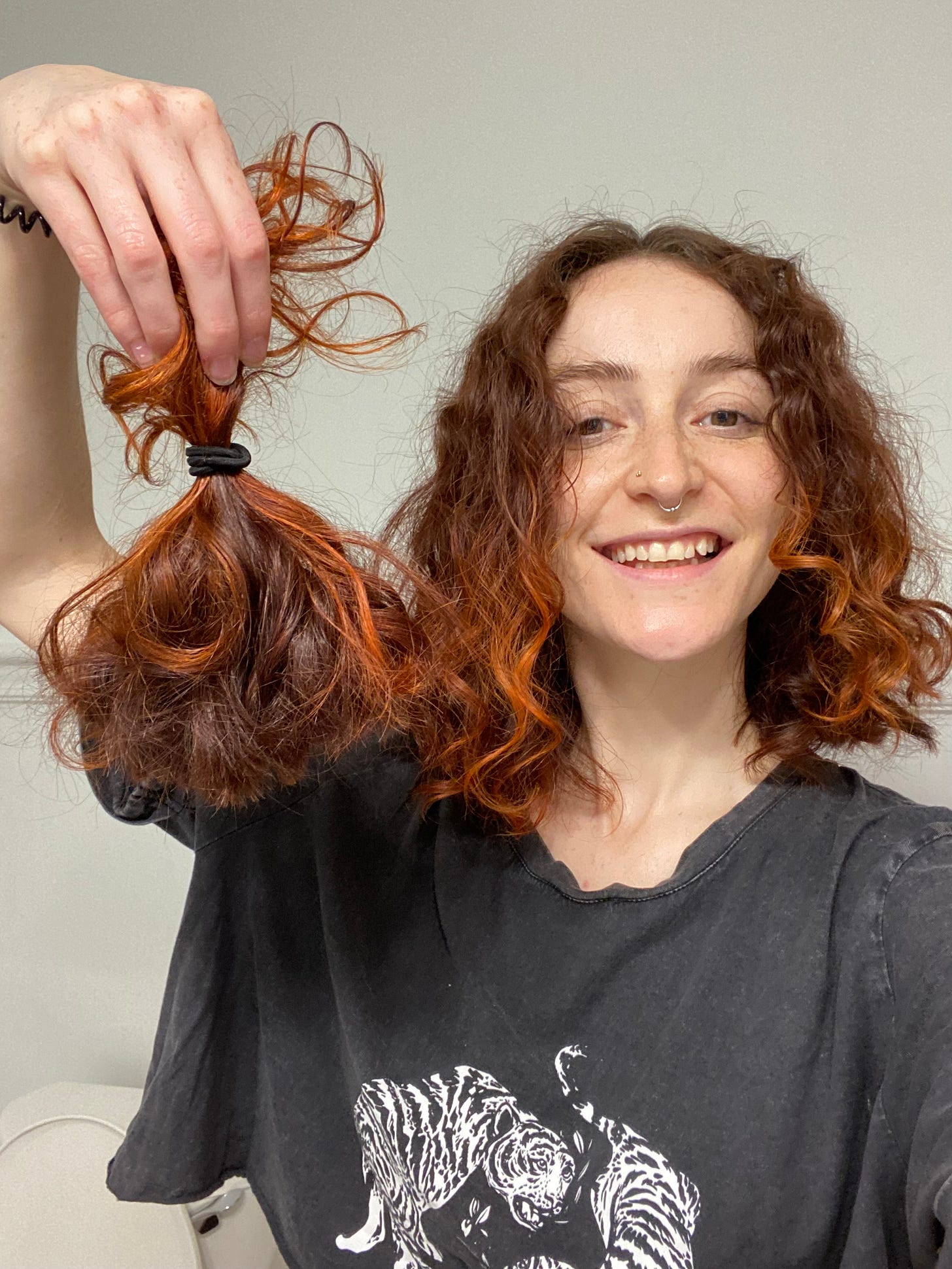 a selfie of Jo grinning widely, holding up a ponytail of freshly chopped hair.