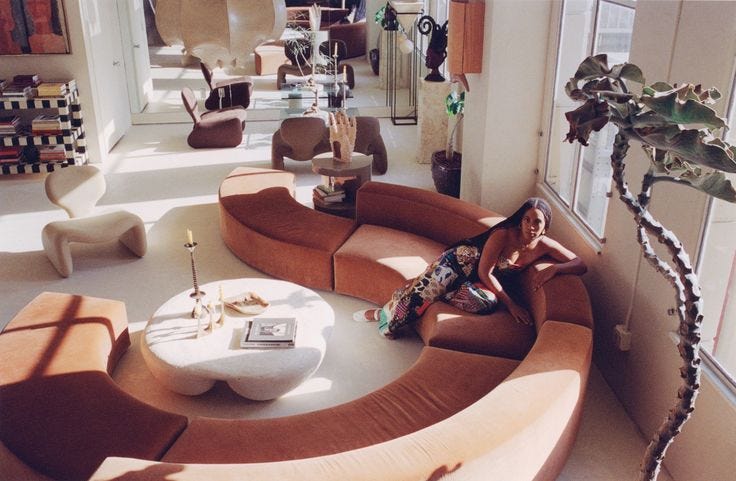 This may contain: a woman sitting on a couch in a room with large windows and lots of furniture