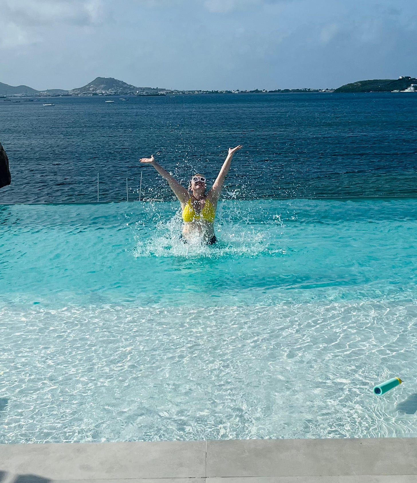 Amber in a pool overlooking the ocean. She has just come up from out of the water. Her hands are in the air and pool water flies around her. Amber in a pool overlooking the ocean. She has just come up from out of the water. Her hands are in the air and pool water flies around her.